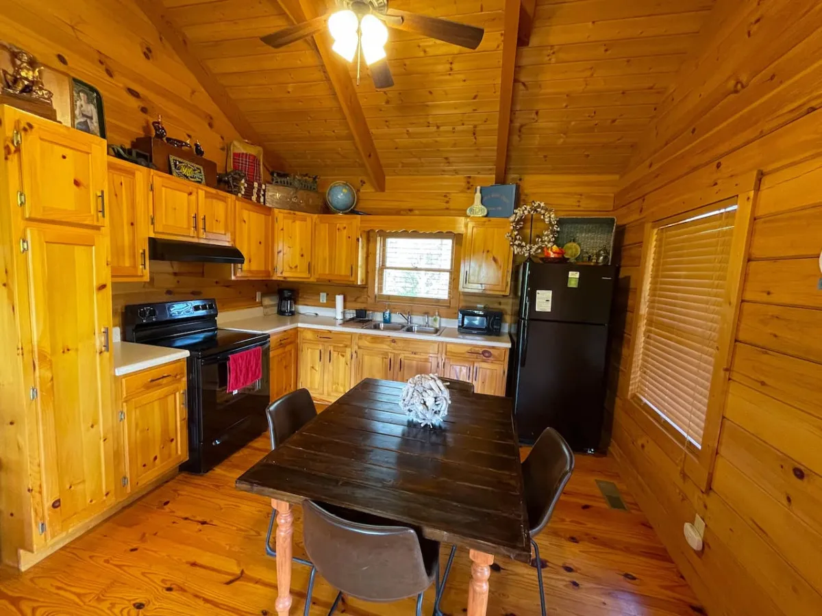 A bright and inviting kitchen and dining area with wooden cabinetry, a spacious dining table, kitchen appliances, and a window letting in natural light. The arrangement highlights the practicality and hominess of the space, ready for family gatherings or casual meals.