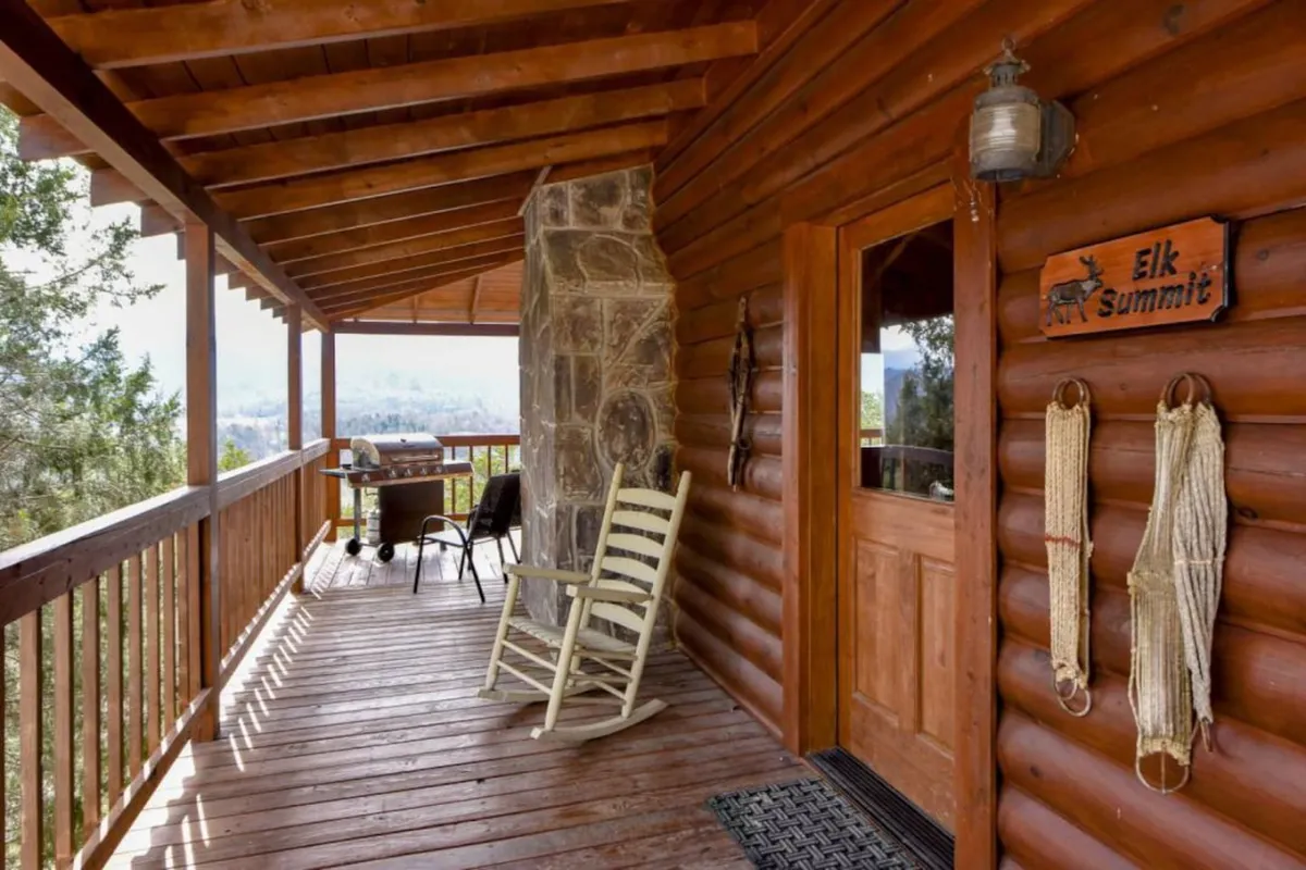 A cozy wooden porch with a rocking chair and a stone fireplace, surrounded by a wooden railing and nestled amidst natural scenery. The soft glow of sunset and the inviting fireplace create an atmosphere of warmth and seclusion.