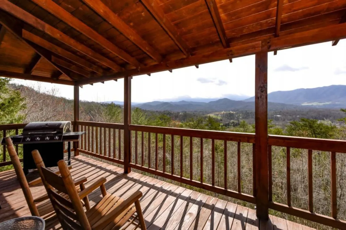 A spacious wooden deck furnished with rocking chairs and a grill, overlooking sweeping mountain views. The deck is ideal for lounging, barbecuing, and soaking up sunrise or sunset vistas, capturing the essence of mountain living in all seasons.