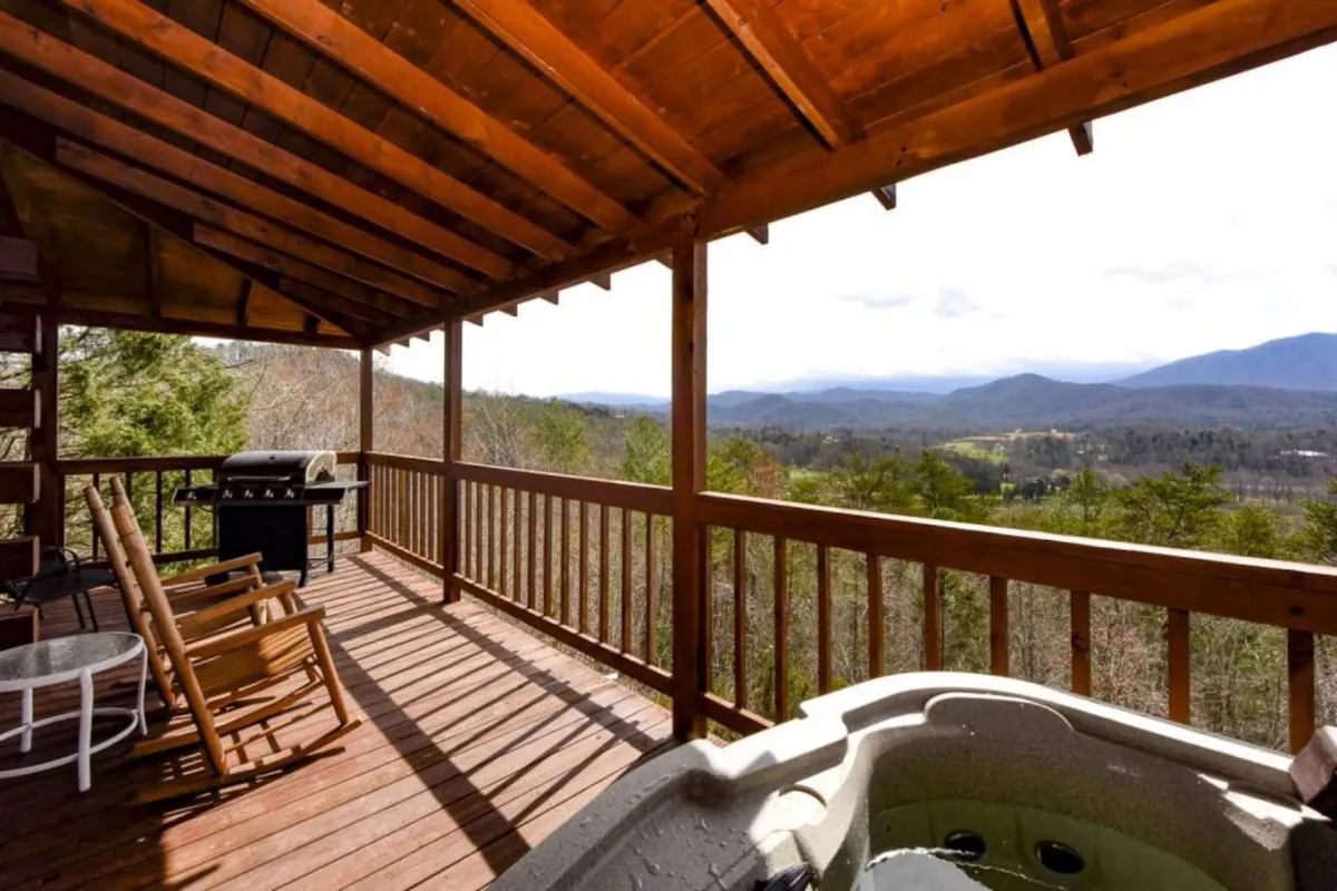 An expansive deck with a hot tub, wooden rocking chairs, grill, and a stunning mountain backdrop. The setup encourages both relaxation and social activities, with ample space for enjoying the outdoors with family, friends, or pets.
