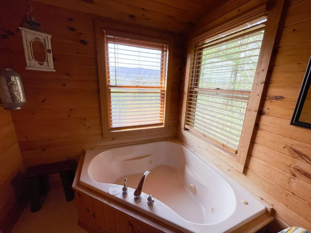 A peaceful bathroom scene featuring a jacuzzi tub set against wooden walls and a window, inviting you to relax while enjoying the natural surroundings outside.