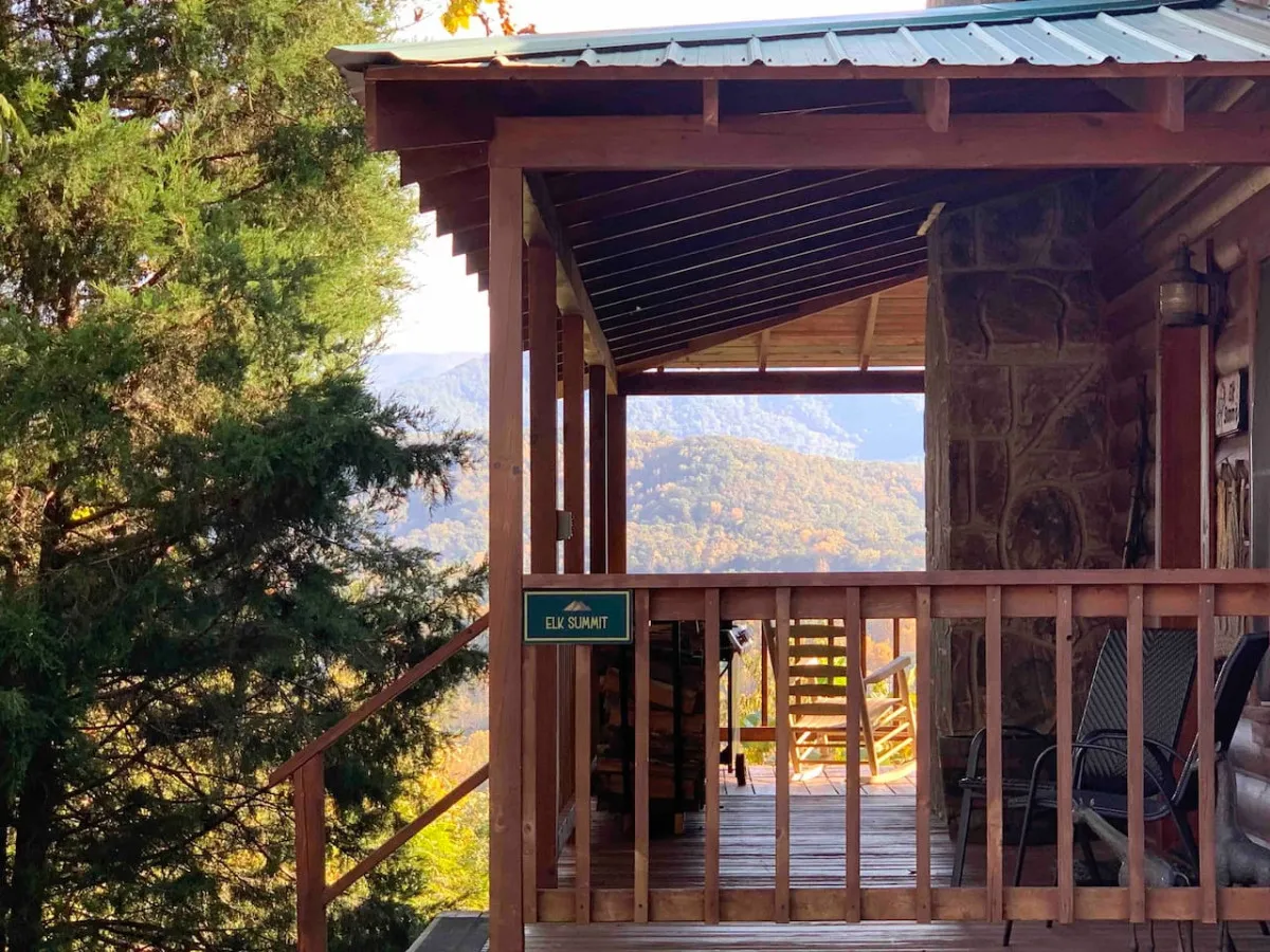 A tranquil wooden deck with rocking chairs, a view of the mountains, and a sign reading 'ELK SUMMIT.' The deck is bathed in soft natural light, perfect for relaxing, socializing, and soaking in the breathtaking scenery at sunrise or sunset.