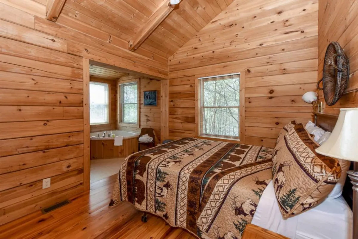 A welcoming interior space with wooden walls, a bed topped by a decorative blanket, a bathtub area tucked nearby, and windows offering tranquil views, evoking a sense of calm and privacy.